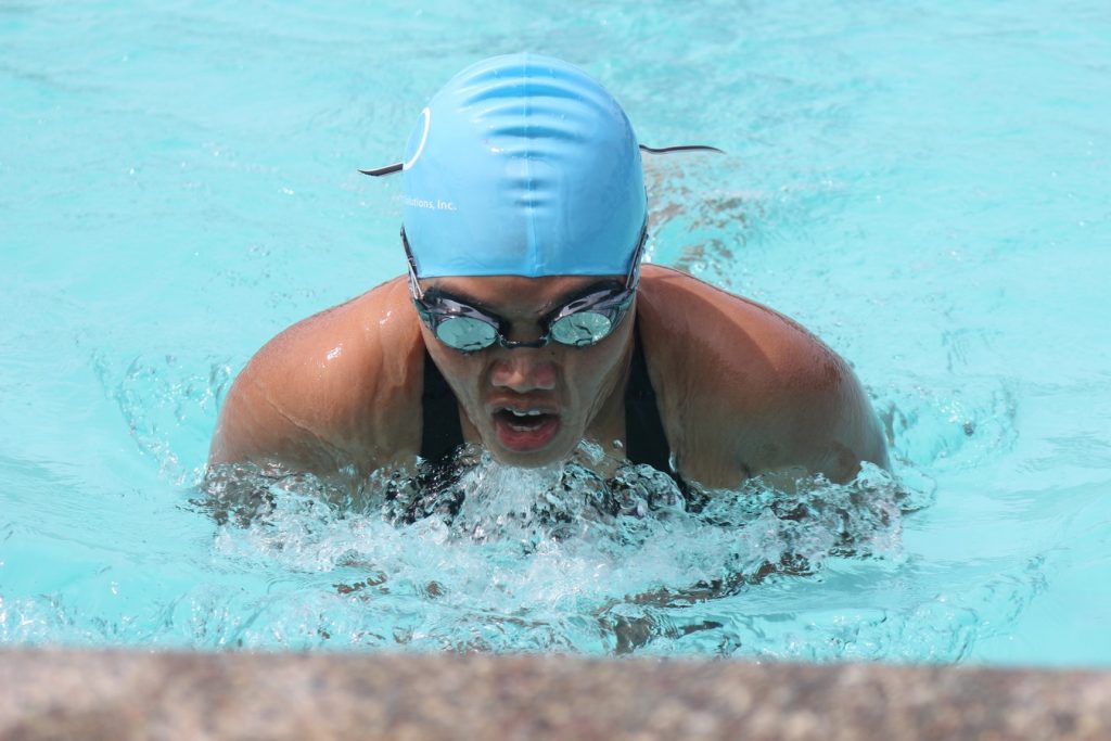 Jeune femme avec un bonnet et des lunettes qui fait de la natation dans sa piscine
